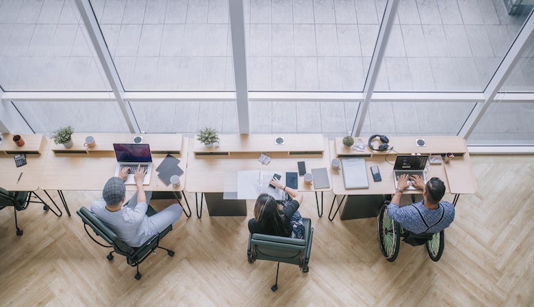 Three people working at an office desk, one is in a wheelchair