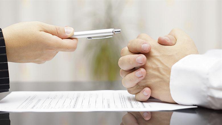 a hand holding out a pen over a contract 