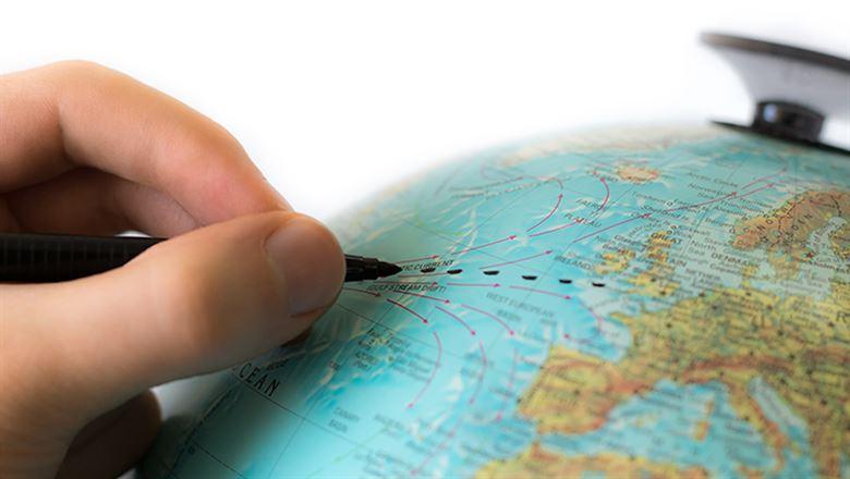 a hand drawing a connecting line on a globe