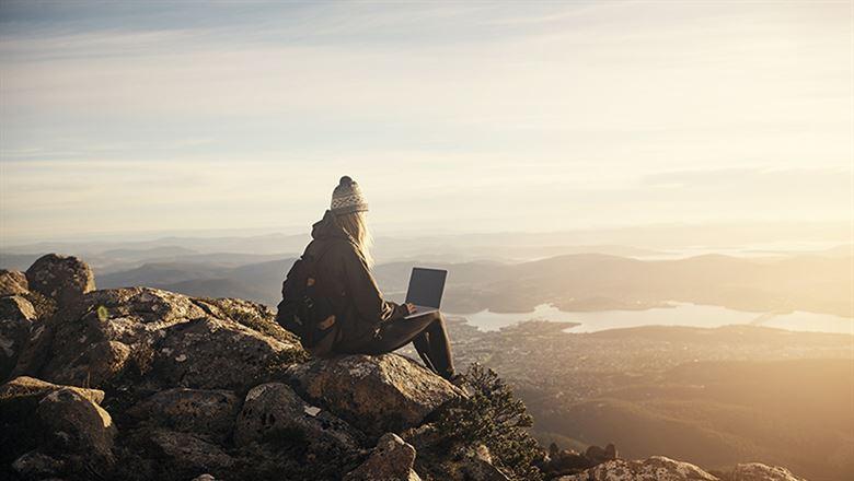 a person using a laptop while looking out over a mountain view