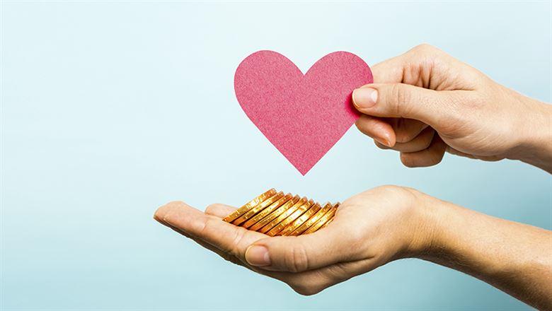 one hand holding gold coins with another hand holding a paper heart