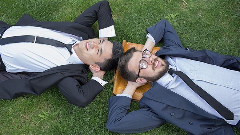 two happy young businessman laying in the grass