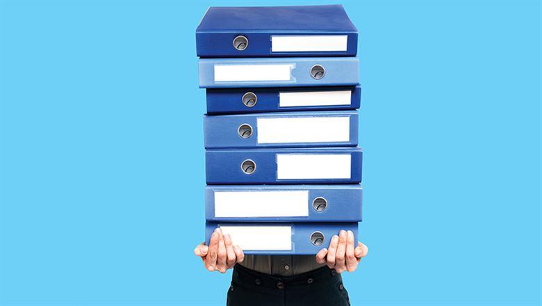 a person struggling to hold up a large stack of binders