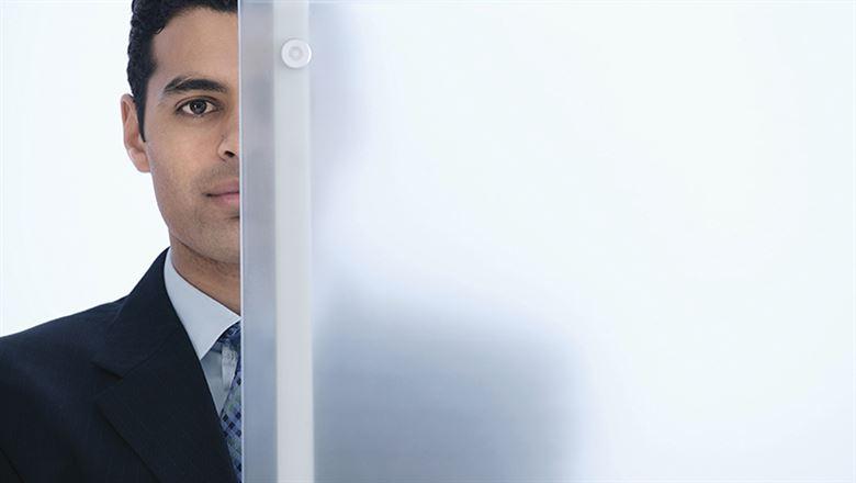 business man standing with half of his face behind a frosted glass