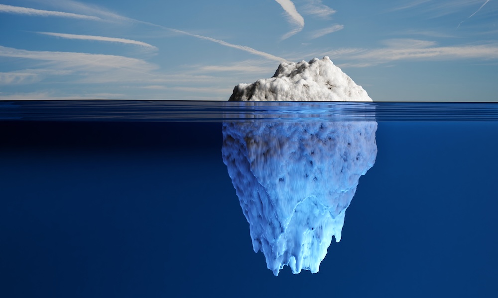 White iceberg exposing small part out of water and hiding most part under the ocean under blue sky.